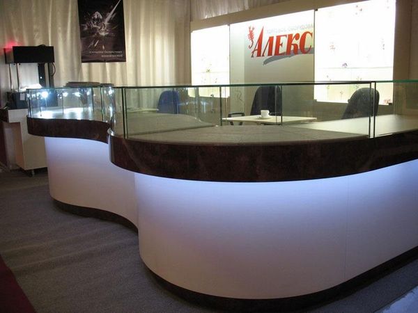 Illuminated curved service counter with a glass riser and the Aleks wordmark on the back wall.