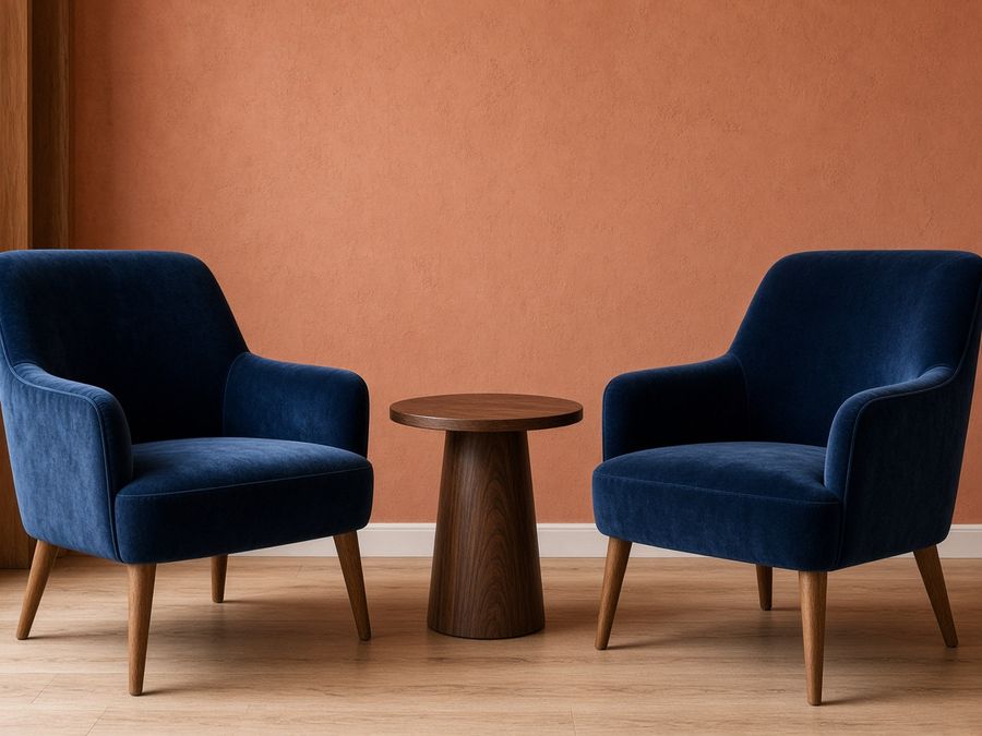 Two navy velvet armchairs with oak legs beside a round walnut table.