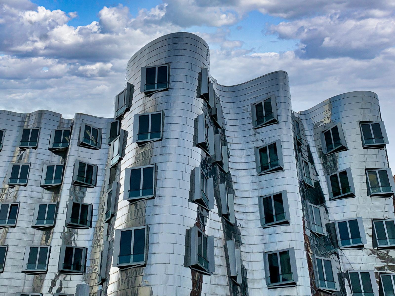 Stainless-steel panel facade with a curved geometry and punched windows, photographed in daylight.