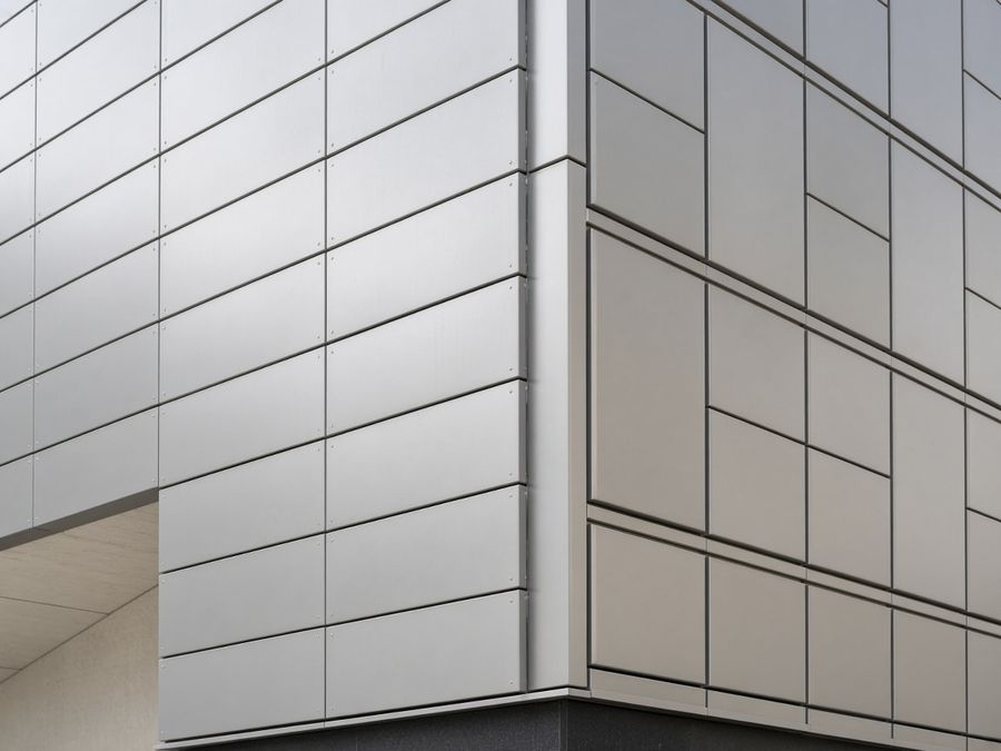 Corner of a commercial building clad in silver-grey aluminum composite panels and aluminum facade cassettes.