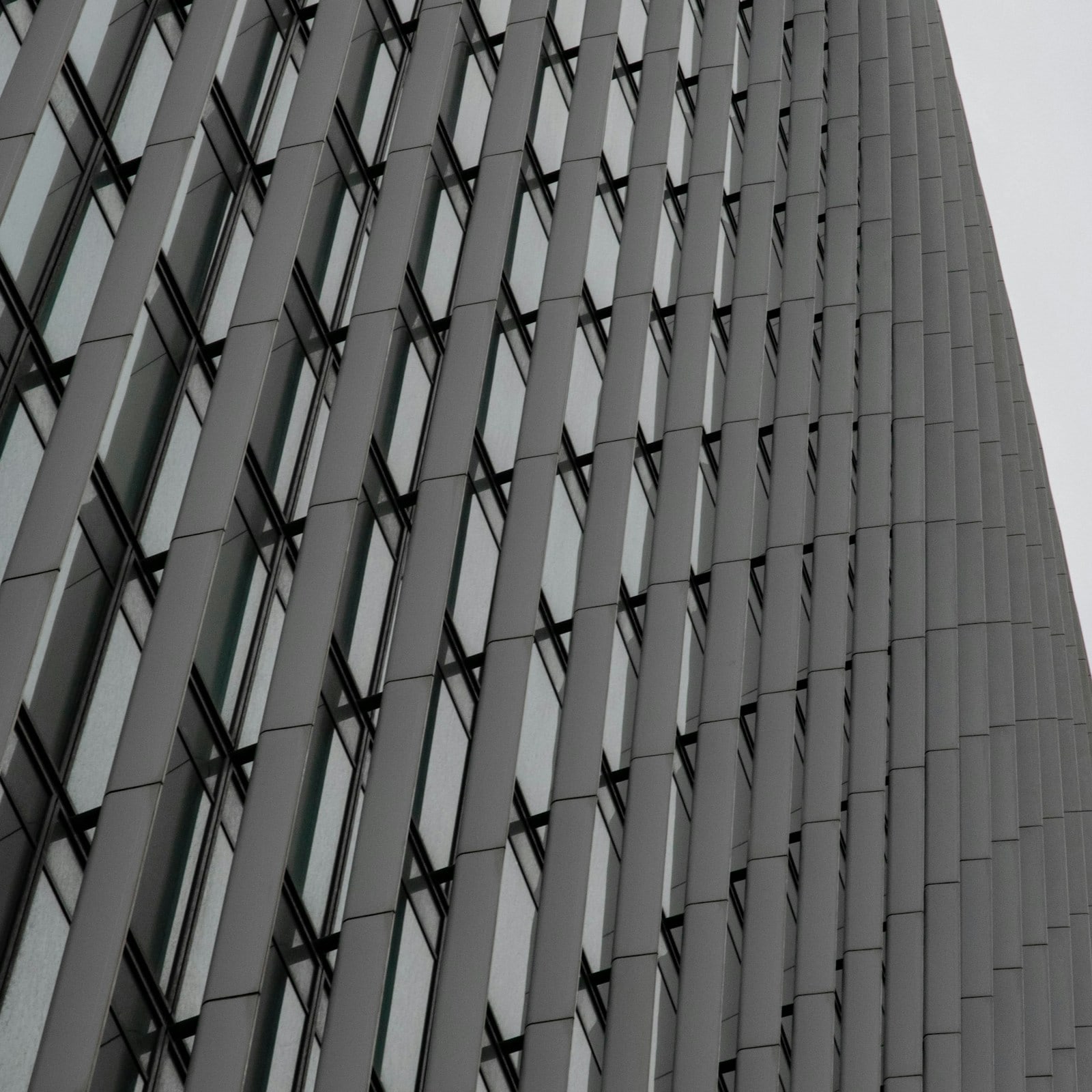 Modern metal-and-glass facade with horizontal panel bands, photographed looking up in daylight.