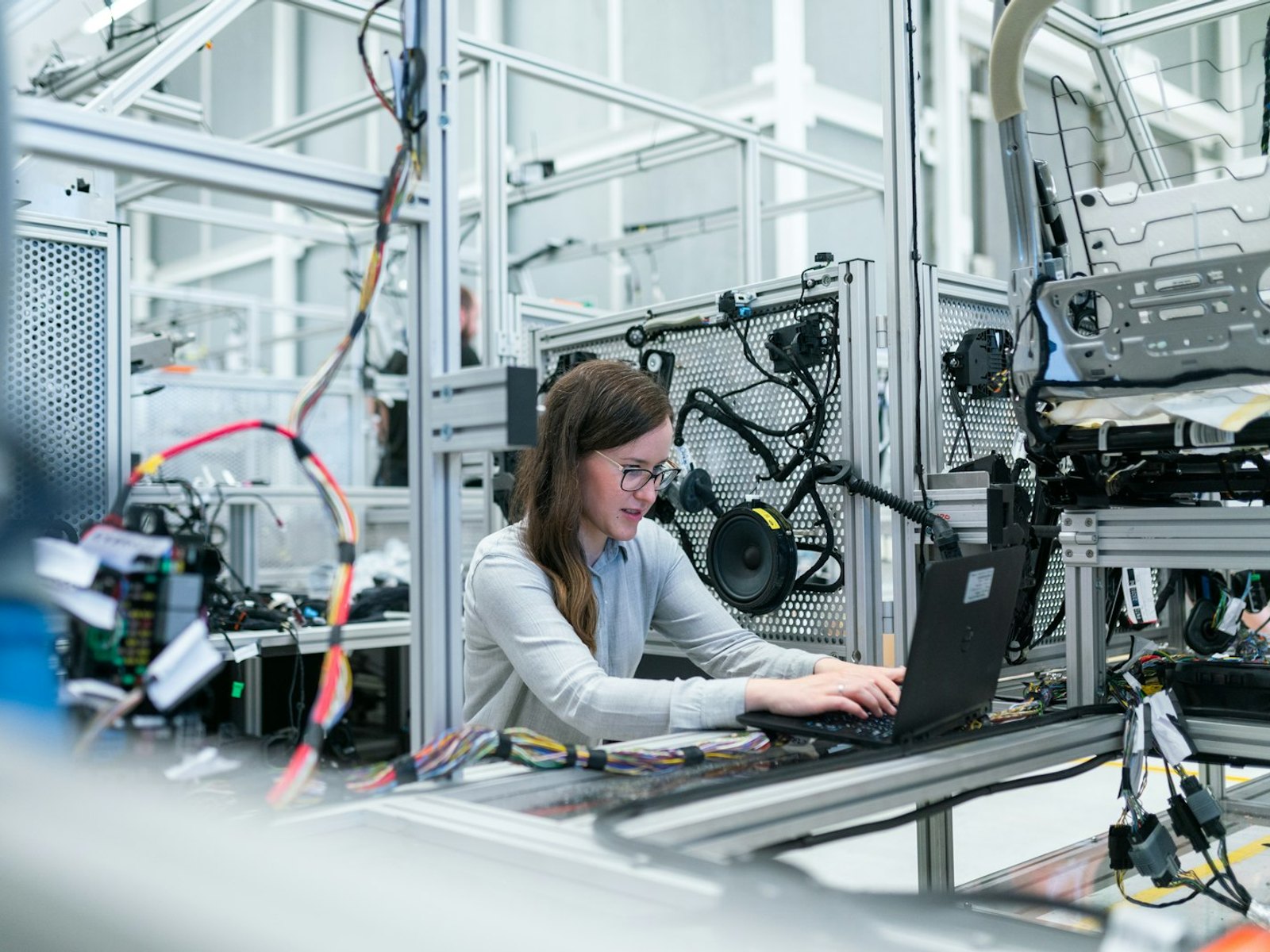 Engineer at a laptop beside industrial assembly equipment and wiring.