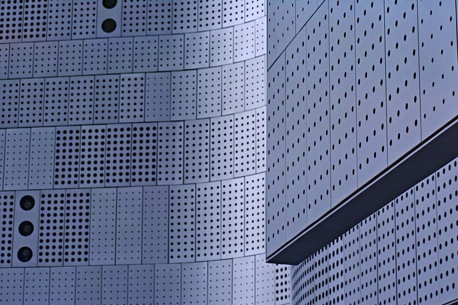 Perforated metal facade panels on a curved building corner, photographed in daylight.